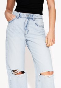 Vaaleansiniset farkut korkealla vyötäröllä, joissa on rento istuvuus, kuluneet polvivammat ja klassinen viiden taskun malli vetoketjulla.