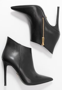 Bottines en cuir noir avec des bouts pointus, des talons aiguilles et une fermeture éclair sur le côté avec des accents dorés. Texture lisse avec un design épuré.