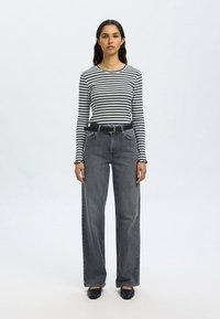 Fekete-fehér csíkos hosszú ujjú felső, magasderekú szürke farmerrel és fekete övvel párosítva. A szett fekete balerinacipővel van kiegészítve.