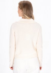 Crème gebreide trui met een geribde kraag en een textuurpatroon, met lange mouwen en een aansluitende zoom. Gestikte details op de mouwen.