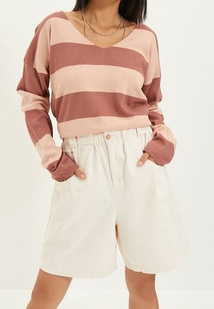 Femme portant un haut à manches longues rayé rose et vieux rose avec un short ample taille haute écru et des colliers en chaîne dorée.