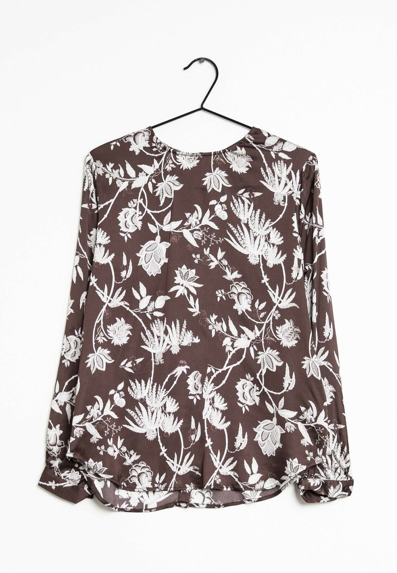 Langärmlige Bluse aus dunkelbraunem Stoff mit weißem Blumenmuster, Boot-Ausschnitt und gerafften Manschetten mit abgerundetem Saum. Hängt an einem schwarzen Haken.