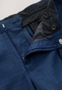 Marineblaue Hose aus strukturiertem Stoff mit Knopf- und Reißverschluss, schwarzem Innenfutter und zusätzlichen Taschen für Funktionalität.