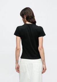 Μαύρο κοντομάνικο μπλουζάκι από μαλακό βαμβάκι, με στρογγυλή λαιμόκοψη και εφαρμοστή γραμμή με λεία υφή. Χωρίς ορατά σχέδια ή διακοσμητικά.