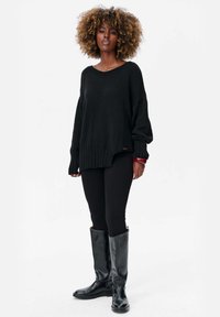 Pull en maille noir surdimensionné avec ourlet côtelé, porté sur des leggings noirs et associé à des bottes noires jusqu'aux genoux. Texture lisse, design décontracté.