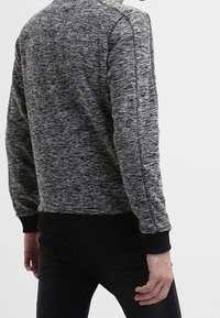 Maglione grigio e nero con texture, dal collo a giro, maniche lunghe e polsini e orlo nero a costine. Il motivo presenta un effetto mélange.