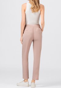 Light pink stretch pants with an elastic waistband, designed with back pockets, tapered leg, and worn with white sneakers.