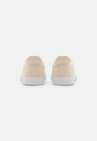 Beige lerret sneakers med hvite gummisåler, med en teksturert finish og en subtil logo preget på bakhæl. 