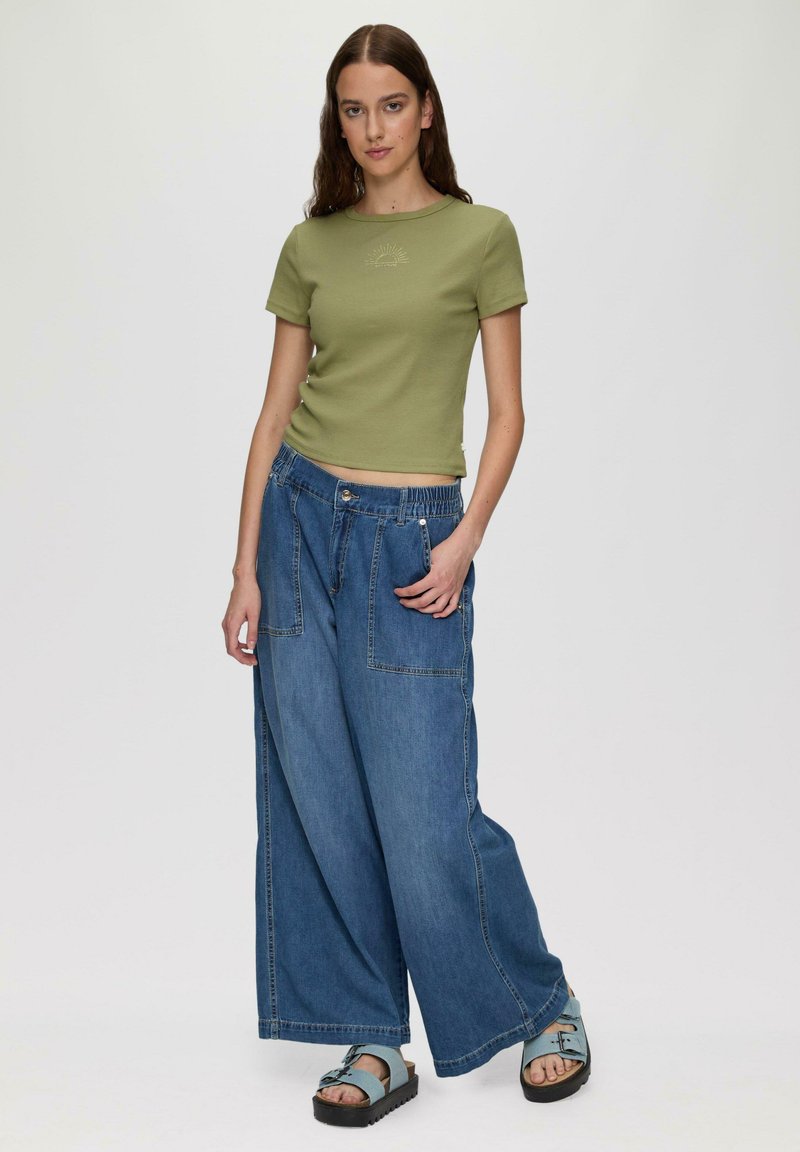 Groen getailleerd shirt met korte mouwen en geborduurde details, gecombineerd met losse blauwe denim broek met grote zakken en een elastische tailleband.