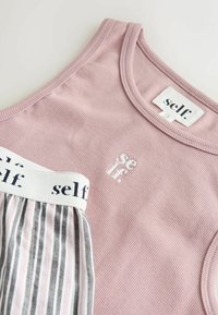 Camiseta sin mangas rosa acanalada con "self." bordado en el pecho, combinada con pantalones a rayas con una cinturilla blanca con el texto "self." impreso.