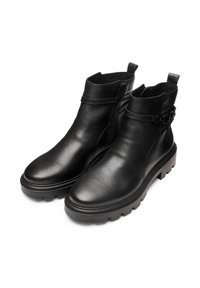 Un paio di stivali neri in pelle alla caviglia con suole spesse, cerniere laterali e cinturini decorativi con fibbie metalliche su uno sfondo bianco.