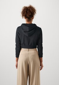 Skórzana czarna bluza z kapturem na sznurku i długimi rękawami, w połączeniu z beżowymi spodniami typu wide-leg o wysokim stanie z tylnymi kieszeniami.