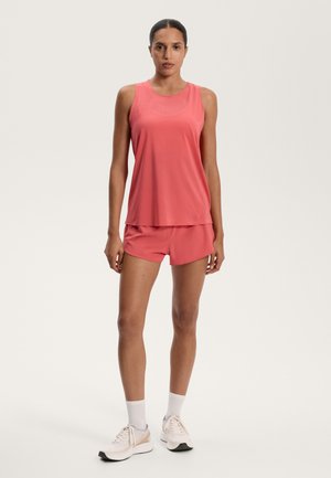 Pink athletic tank top with mesh accents, paired with matching shorts. Features a relaxed fit and moisture-wicking fabric. Light footwear completes the outfit.