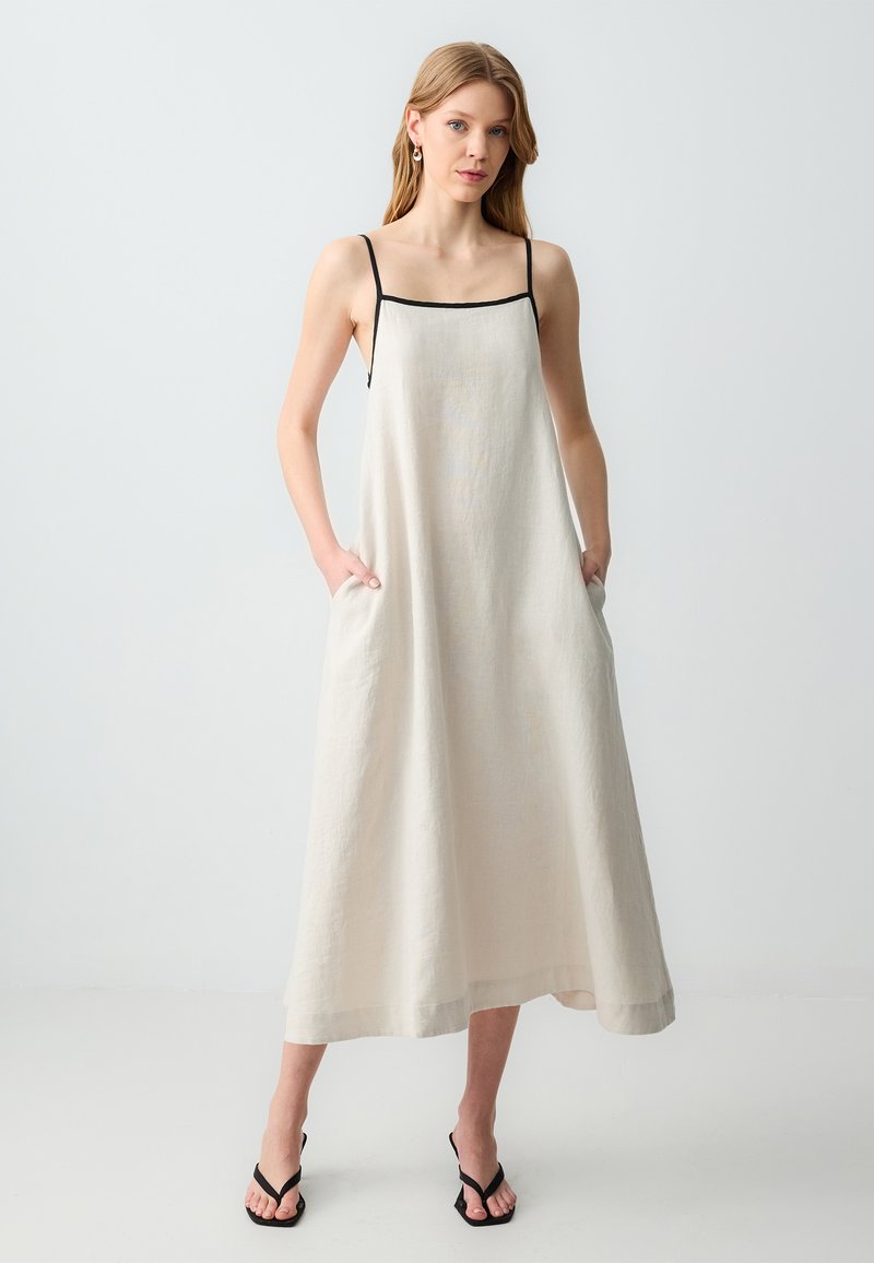 Vestito maxi in lino beige chiaro con spalline nere regolabili, vestibilità rilassata e tasche laterali. Tessuto liscio, lunghezza a pavimento con orlo semplice.