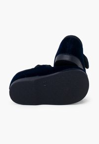 Zapatos de terciopelo azul marino con una superficie texturizada, con suela de goma negra y una correa para un ajuste seguro.