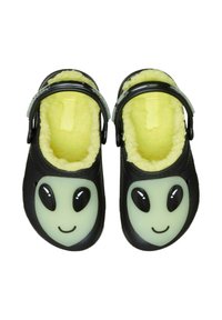 Zoccoli neri con un design di faccia aliena verde luminescente, foderati di morbido giallo e dotati di una fascia regolabile. Forma curvata con superficie esterna texturizzata.
