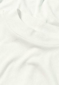 Vit t-shirt i bomull med rundad hals. Har en mjuk, slät textur och ribbad krage. Tyget verkar lätt med lätt fall.