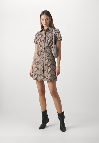 Robe à manches courtes avec boutons en beige ornée d'un imprimé serpent noir, taille cintrée et jupe droite. Associée à des bottines noires et un sac gris.