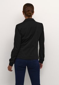 Czarna dopasowana marynarka z długimi rękawami, elegancki design, gładka tekstura i lekko dopasowany krój. Noszona na ciemnoniebieskich dżinsach.