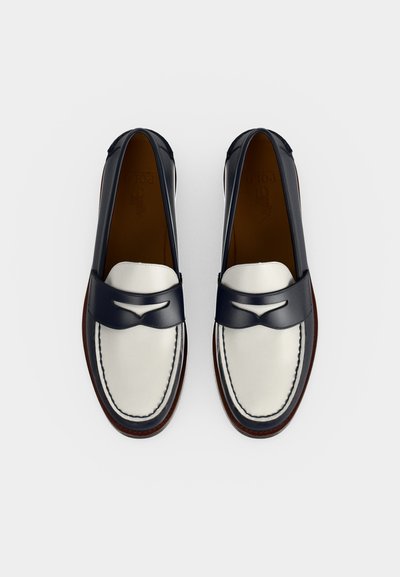 Para czarno-białych skórzanych mokasynów z ciemnym przeszyciem i ozdobną tasiemką na górze, widoczna z góry na białym tle.