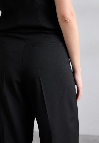 Sorte skræddersyede bukser har et struktureret design med en glat tekstur. En subtil detalje med en baglomme forbedrer den minimalistiske stil.