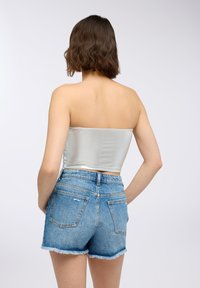 Top corto senza spalline di colore argento con una superficie liscia e lucida, abbinato a pantaloni denim azzurri chiari con orli sfrangiati e tasche posteriori.