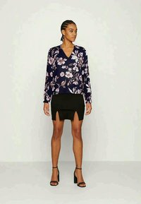 Blusa de manga longa em azul marinho com flores apresenta flores em rosa e branco; combinada com uma saia mini preta com uma fenda frontal; usada com sapatos de salto pretos.