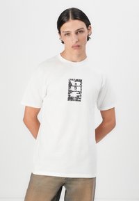 Biele bavlnené tričko s čiernym grafickým motívom v strede obsahujúcim rôzne vzory. Krátke rukávy a okrúhly výstrih, voľný strih.