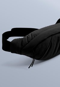 Svart, vadderad midjeväska med strukturerad yta, rundad form, justerbar rem och dragsko för stängning.