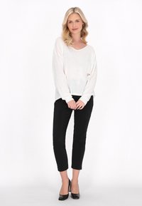 Maglietta bianca a maniche lunghe e scollo a V, abbinata a pantaloni neri aderenti e scarpe nere con tacco alto. Texture liscia con vestibilità comoda.
