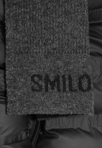Grauer gestrickter Schal mit deutlich sichtbarem "SMILO"-Logo. Weiche Textur, gefaltet, auf einer schwarzen gepolsterten Oberfläche mit geprägten Details.