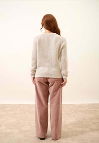 Jasnoszary sweter robiony na drutach z fakturowym wzorem, sparowany z luźnymi różowymi spodniami z korduroyu, widok z tyłu na jednolitym tle.