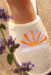 Wool felt slipper in beige with a colorful sunburst embroidery design featuring orange, yellow, and purple accents; white text below reads "SONNENSCHLEI."