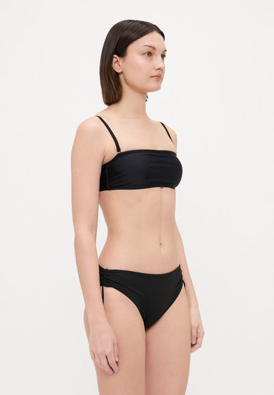 Conjunto de bikini negro que incluye un top bandeau con tirantes finos ajustables y pantalones de tiro bajo con fruncidos en los lados. Textura de tela suave.