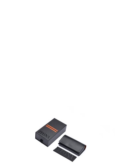 Svart läderfodral med präglad logotyp, placerad bredvid en svart låda med en orange rand och samma logotyp, mot en vit bakgrund.