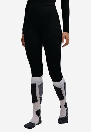 Gambe che indossano leggings neri aderenti e calzini bianchi al ginocchio con motivi geometrici neri e grigi.