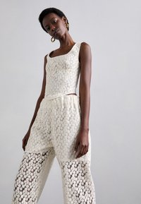 Lace to-delt sett i elfenben, med en tettsittende tank topp med lomme og vide bukser med gjennomsiktig blomsterdetaljering.
