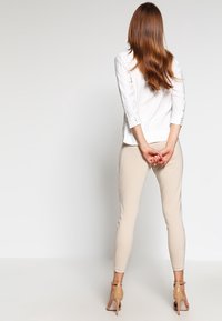 Vit blus med små prickar, trekvartslång ärm och knappdetaljer. Beiga slim-fit byxor och nakenklackar. Bakifrån.