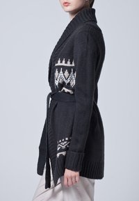 Dziergany kardigan w ciemnoszarym kolorze, z wzorzystym kremowym motywem na klatce piersiowej. Posiada pasek i szerokie prążkowane mankiety.