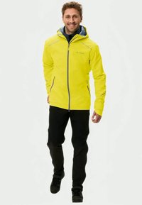 Yellow waterproof jacket with a zippered front, adjustable hood, and gray accents, paired with black pants and sturdy footwear.