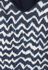 Haut en tissu sans manches présentant un motif en zigzag bleu marine et blanc. La texture est côtelée avec un léger éclat. Encolure arrondie.