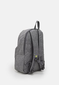 Gray fabric backpack with a rounded shape, zip closure, adjustable straps, and a front pocket. Features a small green logo accent.