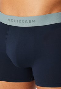 Boxer blu navy con una fascia elastica grigio chiaro che presenta il nome del marchio "SCHIESSER" in un motivo discreto. Tessuto dalla trama liscia.