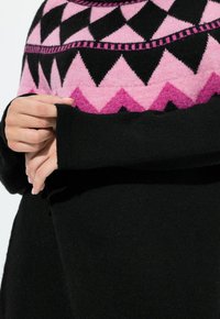 Maglione nero a maglia con yoke a motivo in rosa e nero con design a zigzag. Le maniche sono allungate, mostrando una texture morbida e dettagli raffinati.