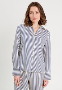 Chemise à rayures bleu et blanc, avec un col, des manches longues et une coupe ample. Tissu texturé avec des rayures verticales.