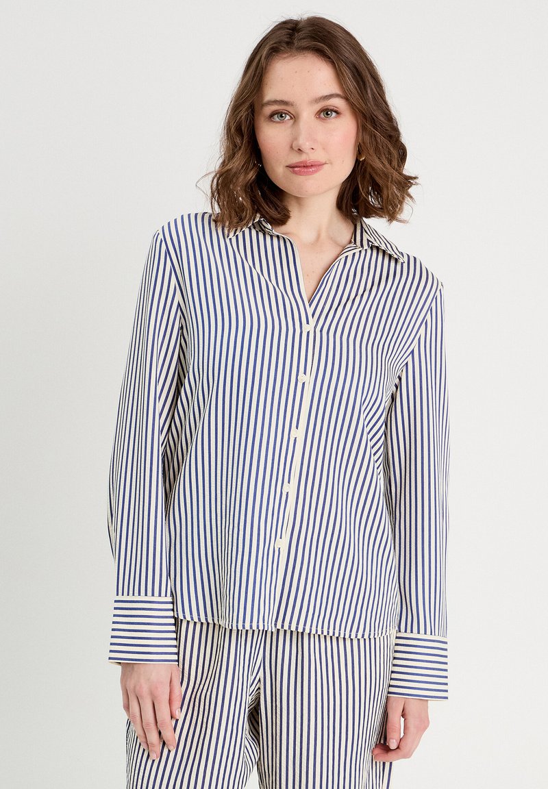 Chemise à rayures bleu et blanc, avec un col, des manches longues et une coupe ample. Tissu texturé avec des rayures verticales.