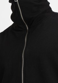 Felpa nera con zip, dotata di un colletto alto, texture liscia e chiusura con zip metallica. Design semplice, senza ulteriori motivi o dettagli.