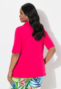 Fuchsia polo shirt met korte mouwen, een zachte textuur en een ontspannen pasvorm, gecombineerd met kleurrijke tropische print broek met verschillende bladmotieven.