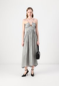 Abito maxi grigio senza maniche con corpino arricciato e spalline sottili. Abbinato a tacchi neri con cinturino alla caviglia e una piccola borsa nera.