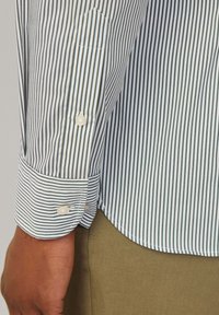 Camicia a maniche lunghe a righe con strette strisce verticali blu e bianche, dotata di polsini a punta e due chiusure con bottoni. Tessuto dalla superficie liscia.